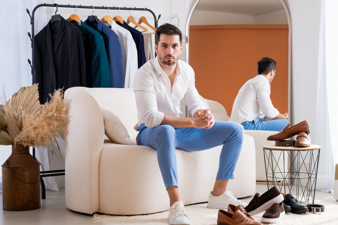 A fashionable man in a modern showroom with elegant outfits and shoes displayed around him.